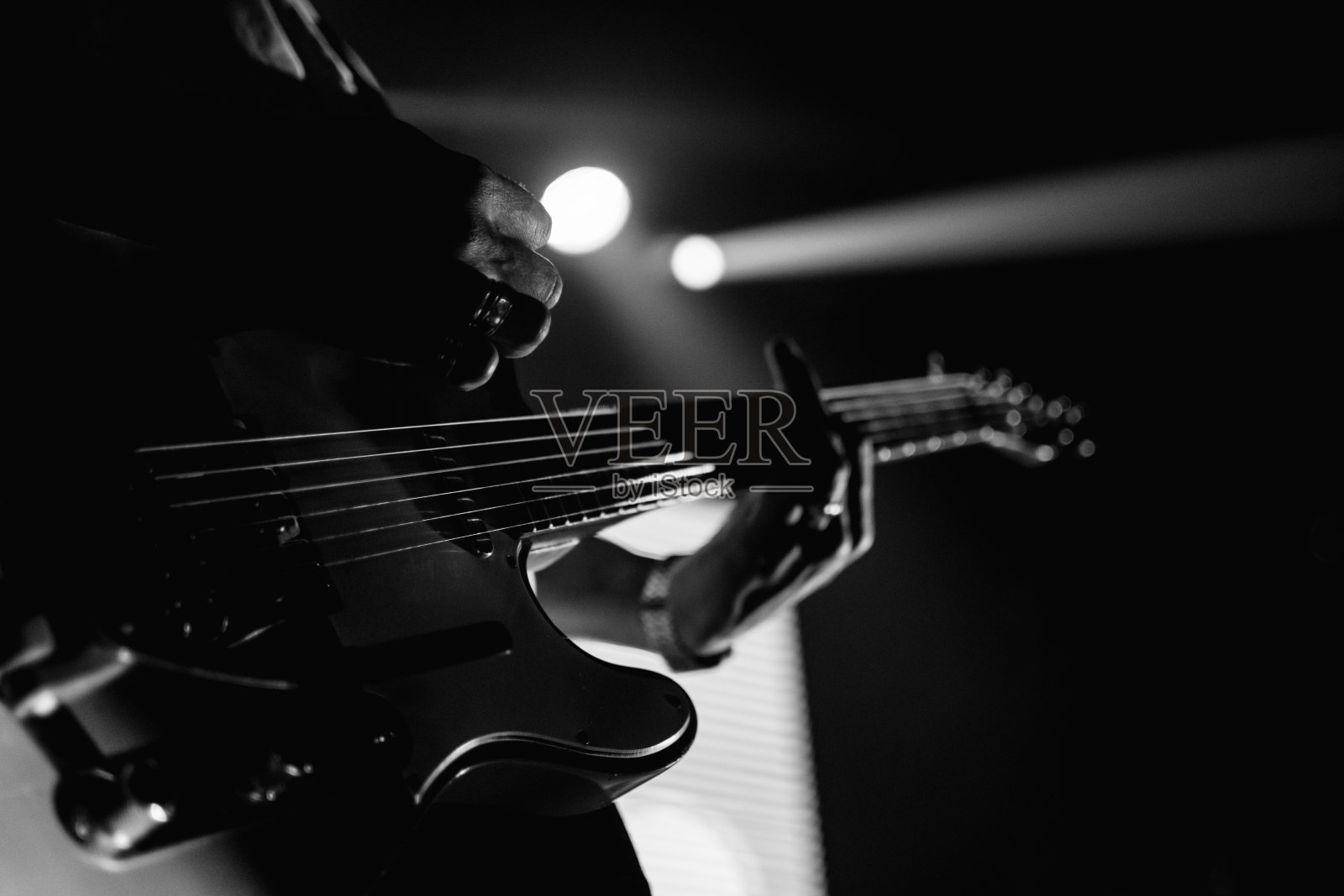 一个吉他手表演现场的特写。手，吉他指板，弦在深的黑色和白色音调。照片摄影图片