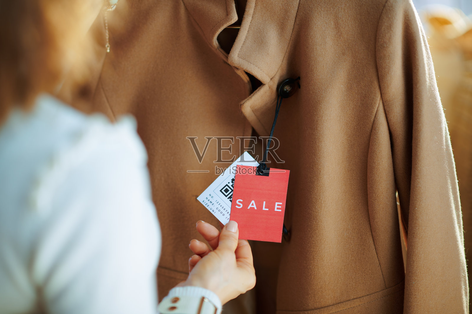 近距离观察时尚女性检查米色大衣的价格标签照片摄影图片