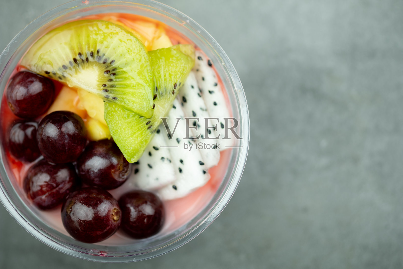 健康早餐塑料碗冷冻酸奶冰沙，新鲜水果，猕猴桃，葡萄和火龙果切片。照片摄影图片