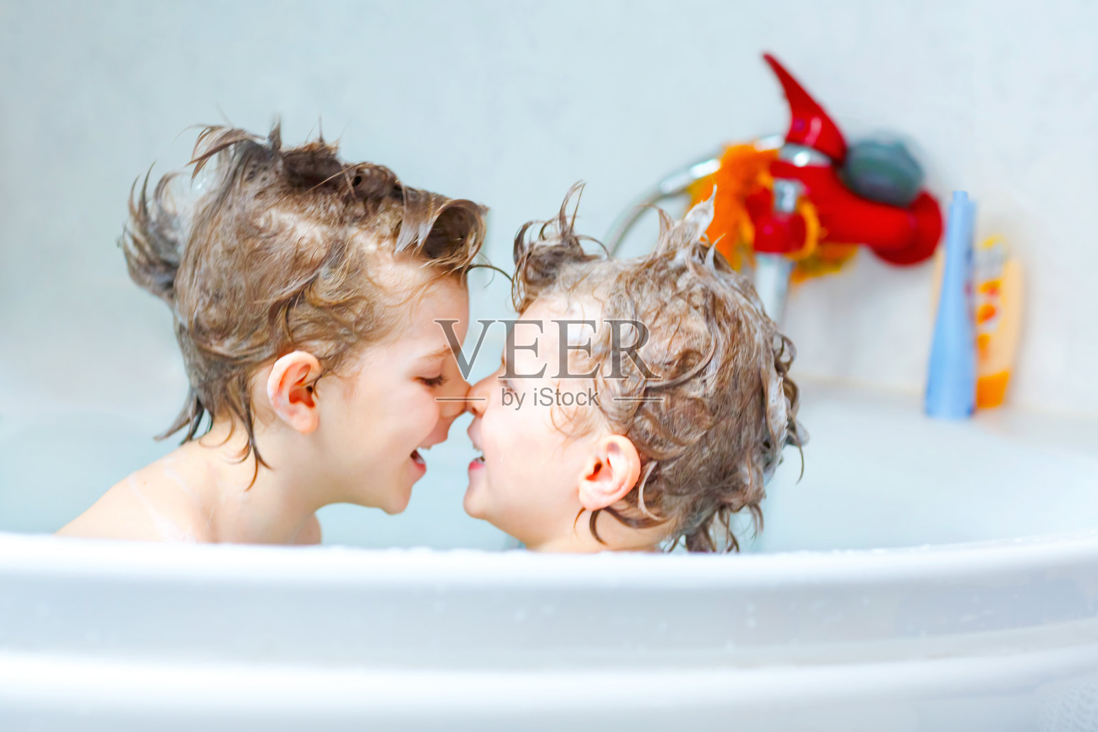 快乐的兄弟姐妹:两个健康的小双胞胎在家里的浴缸里和水一起玩耍。孩子们在一起玩得很开心。儿童用香波洗头和头发。照片摄影图片