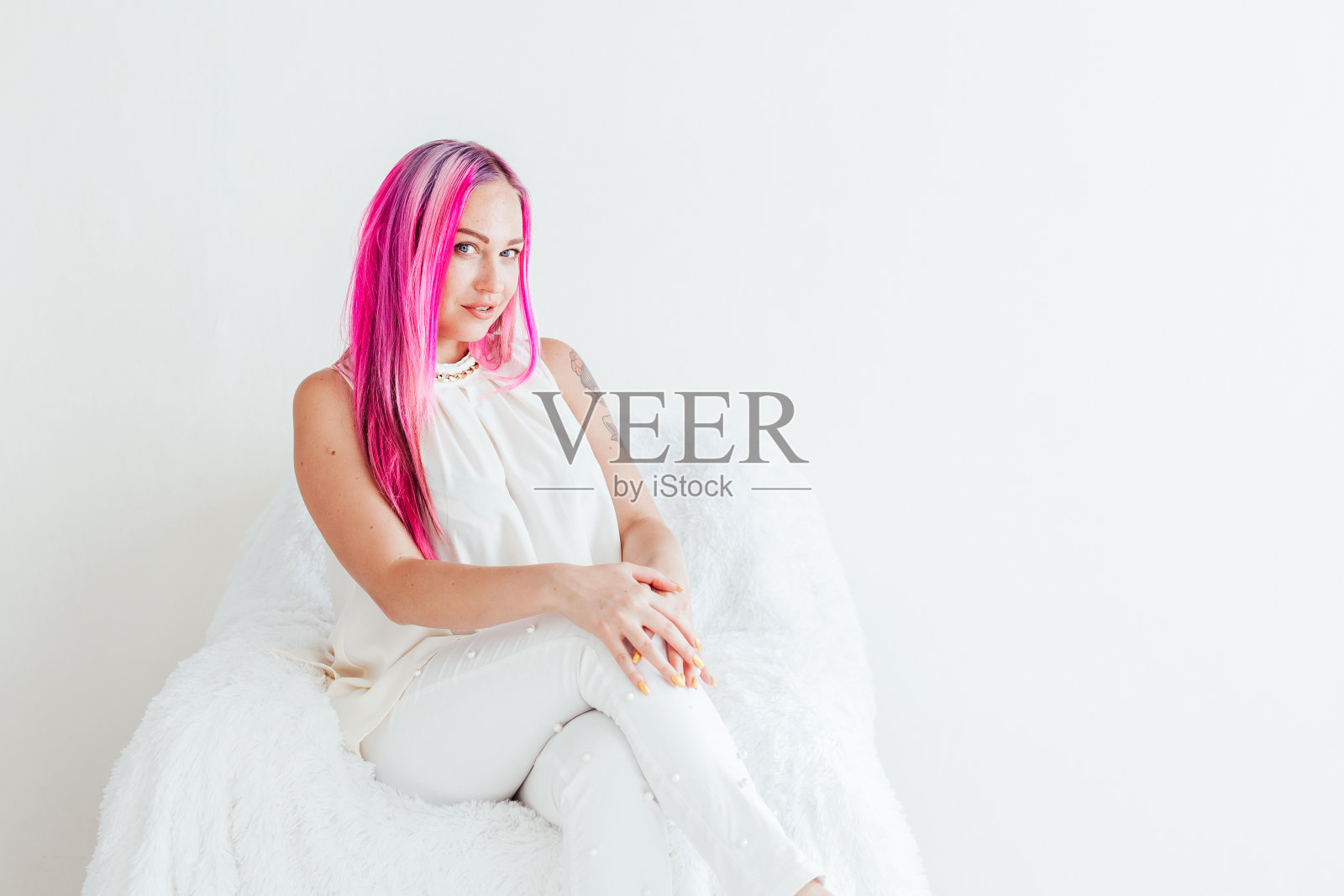 在一间白色的房间里，一个粉红头发的女孩坐在椅子上照片摄影图片