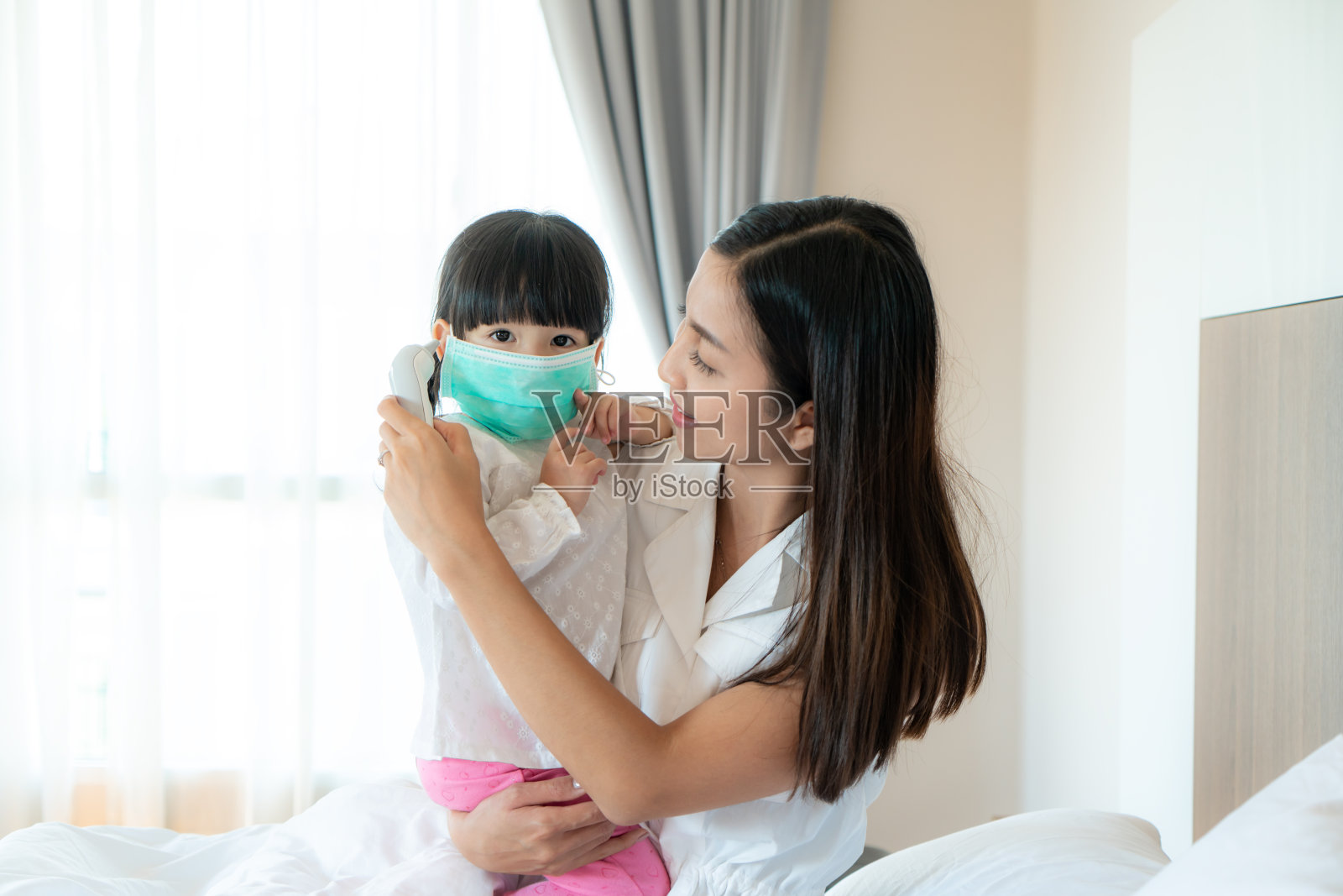 亚洲年轻的母亲检查测量她生病的小女儿的温度感觉像发烧或流感在卧室在家里。人们生病的视觉效果，以及遭受流感、头痛和普通感冒等常见疾病的痛苦。照片摄影图片