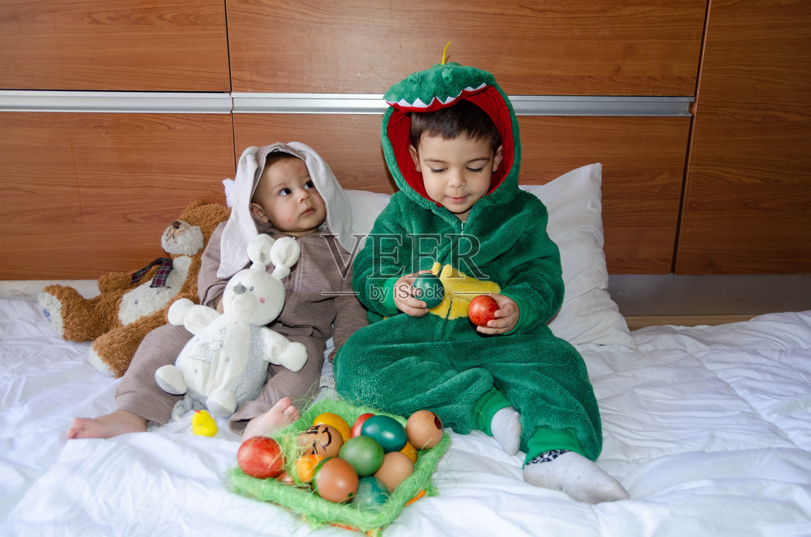 可爱的兄弟姐妹们穿着兔子和恐龙的服装玩着彩色的复活节彩蛋。Wgg狩猎和童年照片摄影图片