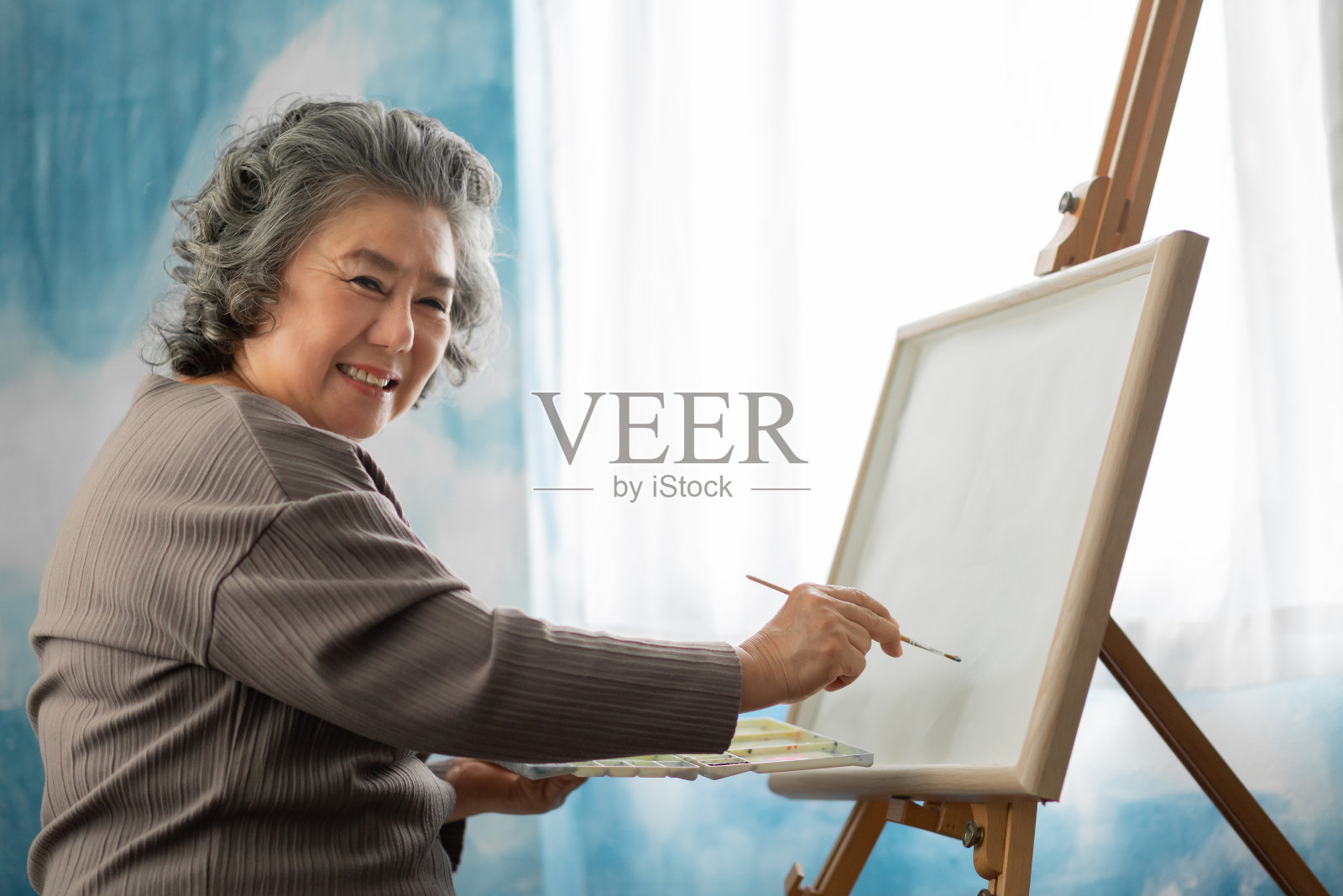 快乐微笑的亚洲老妇人油画在画布上的房子在假日。照片摄影图片