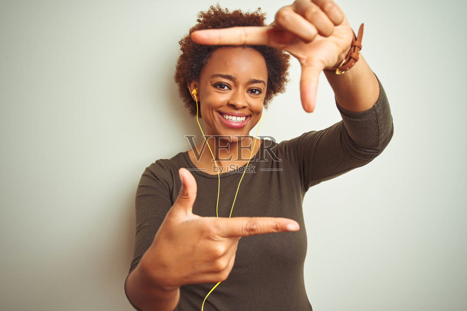 非洲裔美国妇女戴着耳机听音乐在孤立的背景微笑做框架与手和手指与快乐的脸。创意和摄影概念。照片摄影图片