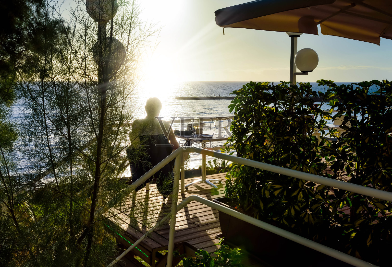 一个男人坐在阳台上看大海上的日落照片摄影图片