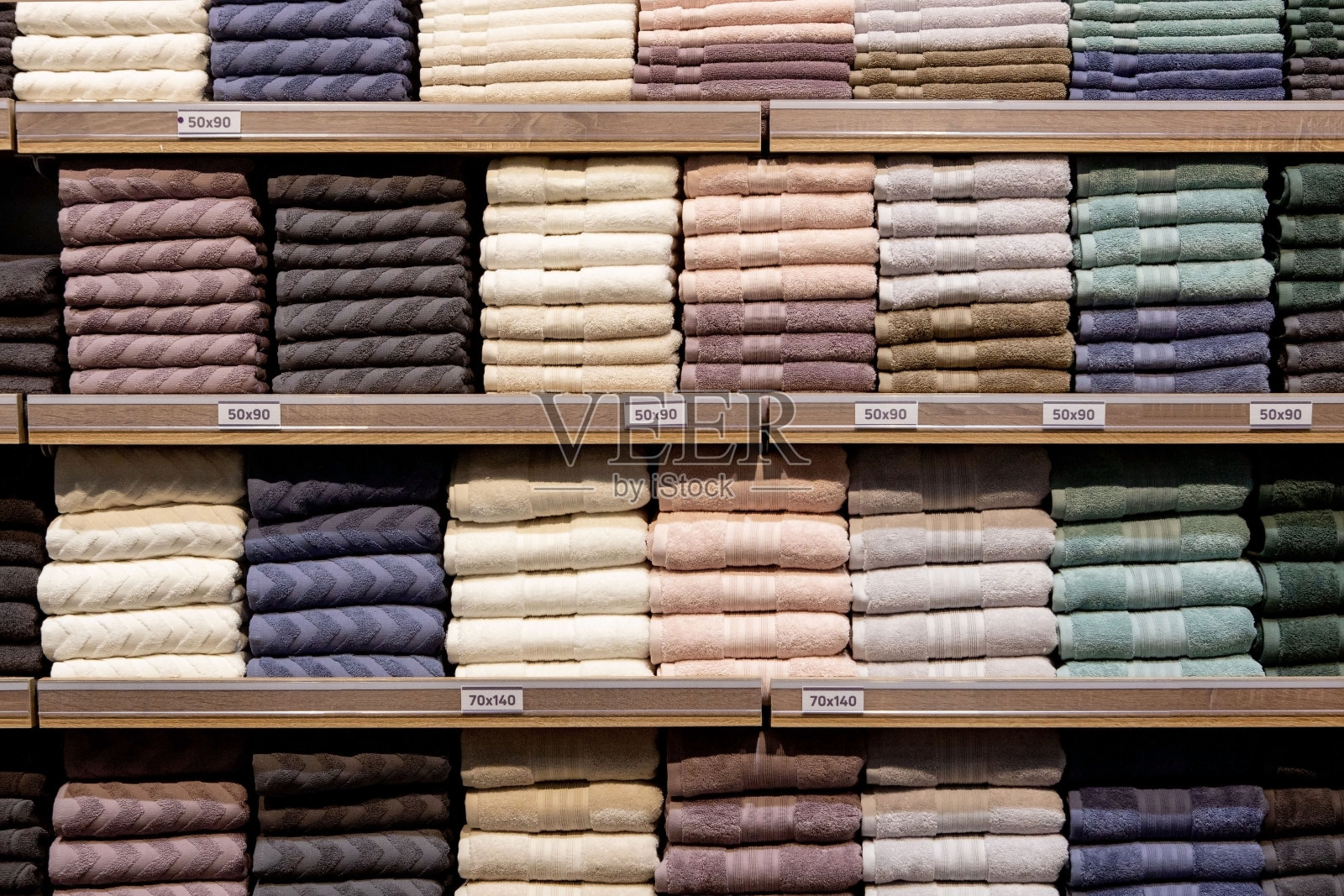 折叠的五彩毛巾放在架子上。叠得整整齐齐的衣服。衣架上的衣服保暖。折叠整齐的棉布毛巾照片摄影图片