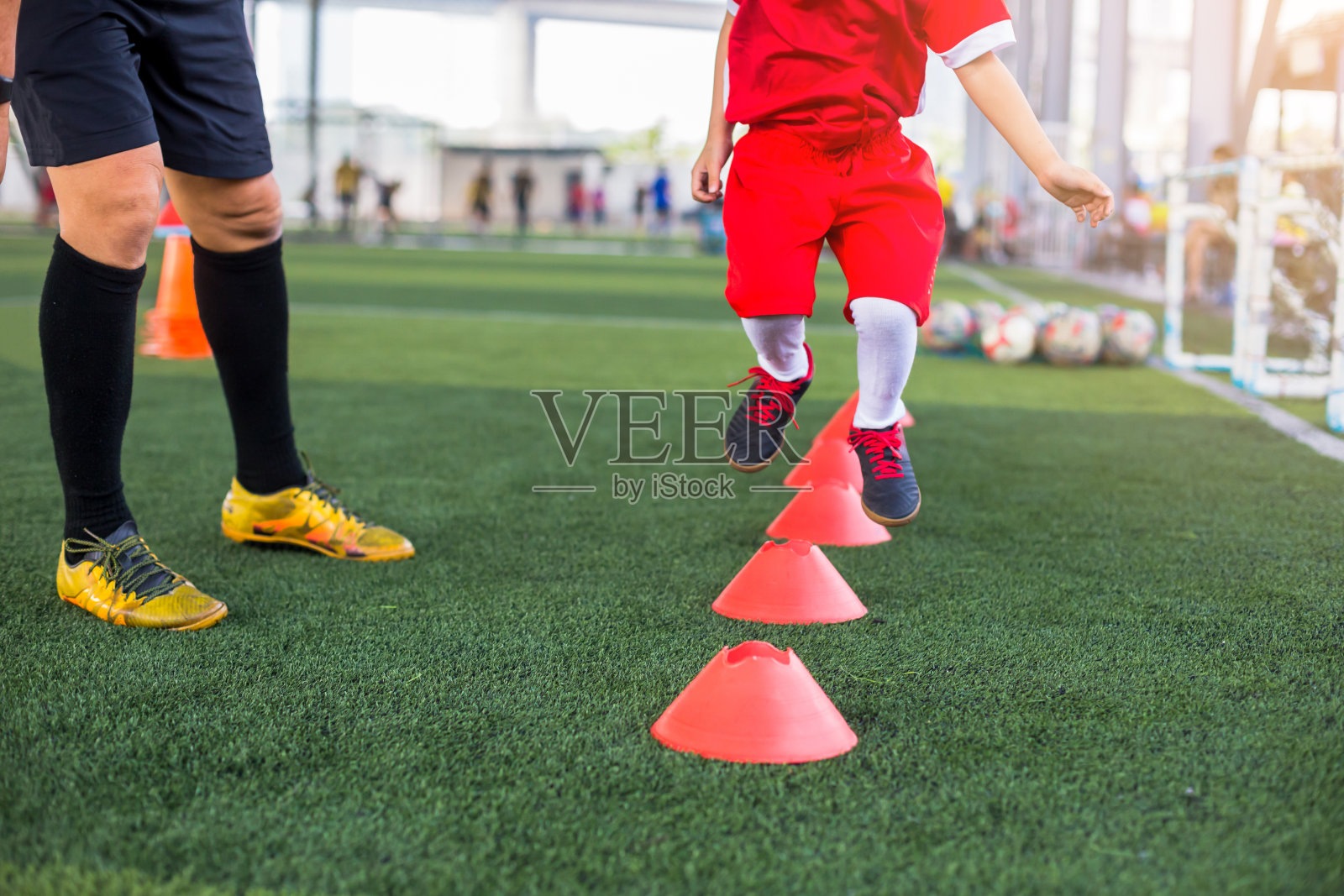 孩子足球慢跑和跳跃之间的圆锥标记与教练站在足球学院教练。照片摄影图片