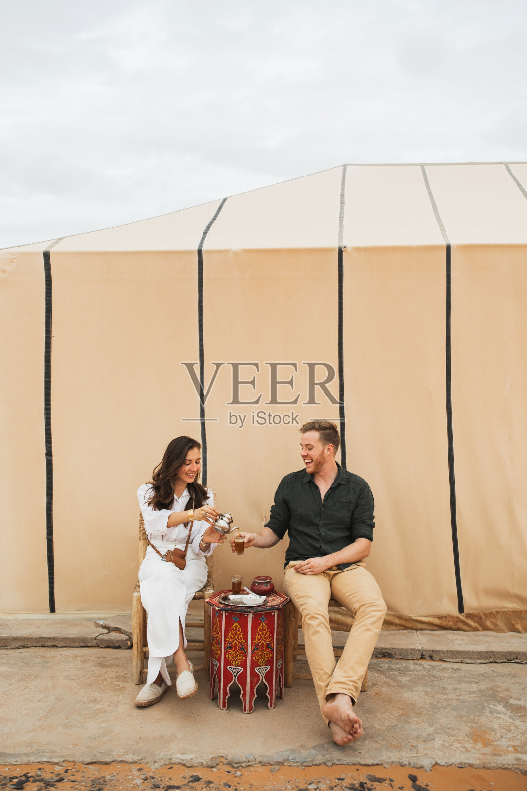 年轻幸福的夫妇在摩洛哥的撒哈拉沙漠野营中享受传统的摩洛哥薄荷茶。照片摄影图片