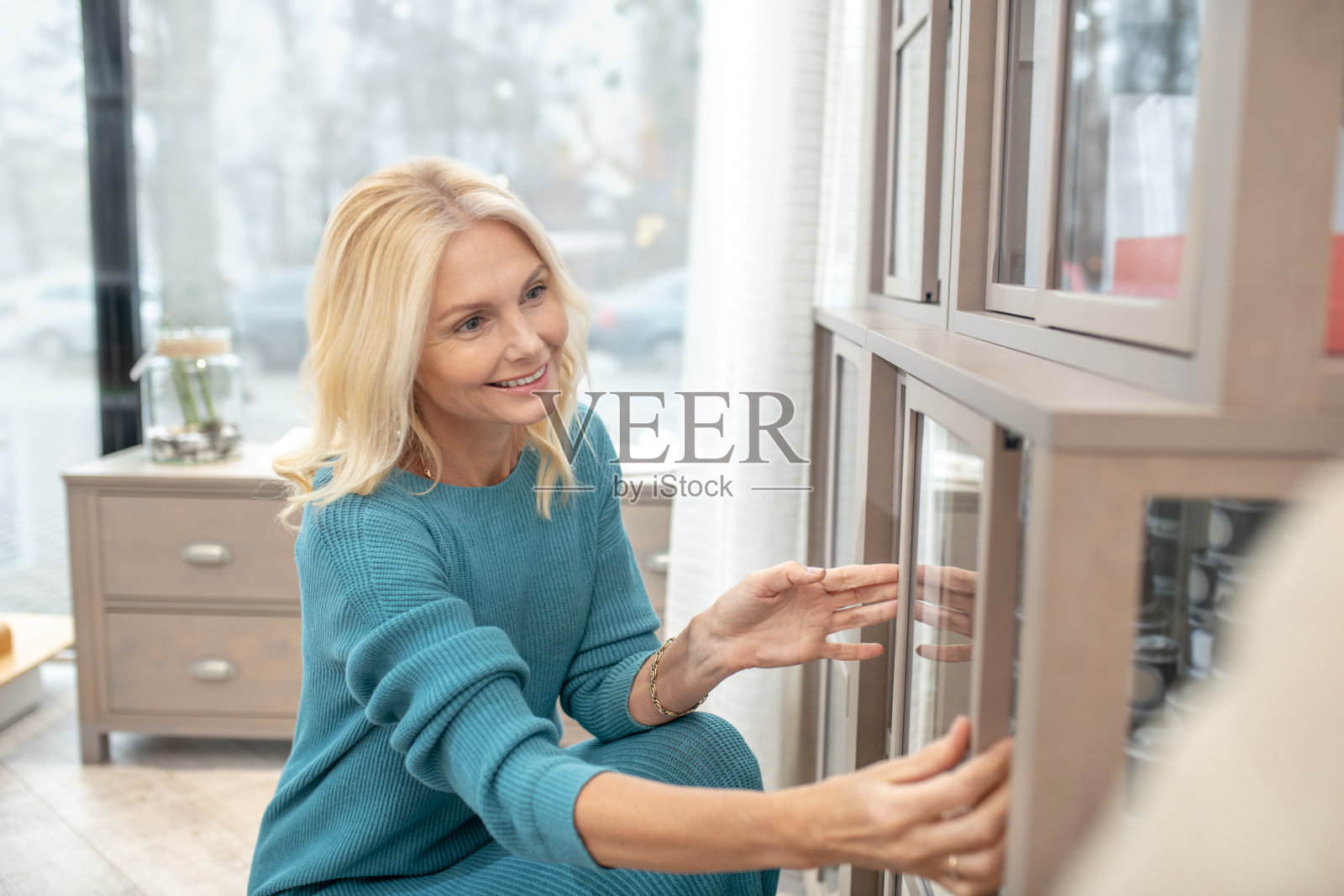 一个感兴趣的女人蹲在玻璃柜旁。照片摄影图片