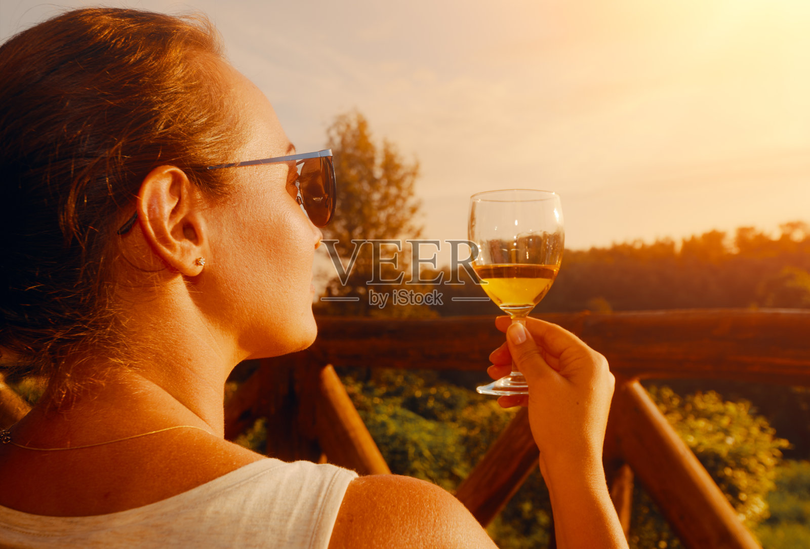 快乐的女人拿着杯子，坐在阳台上享受美味的饮料在日落照片摄影图片