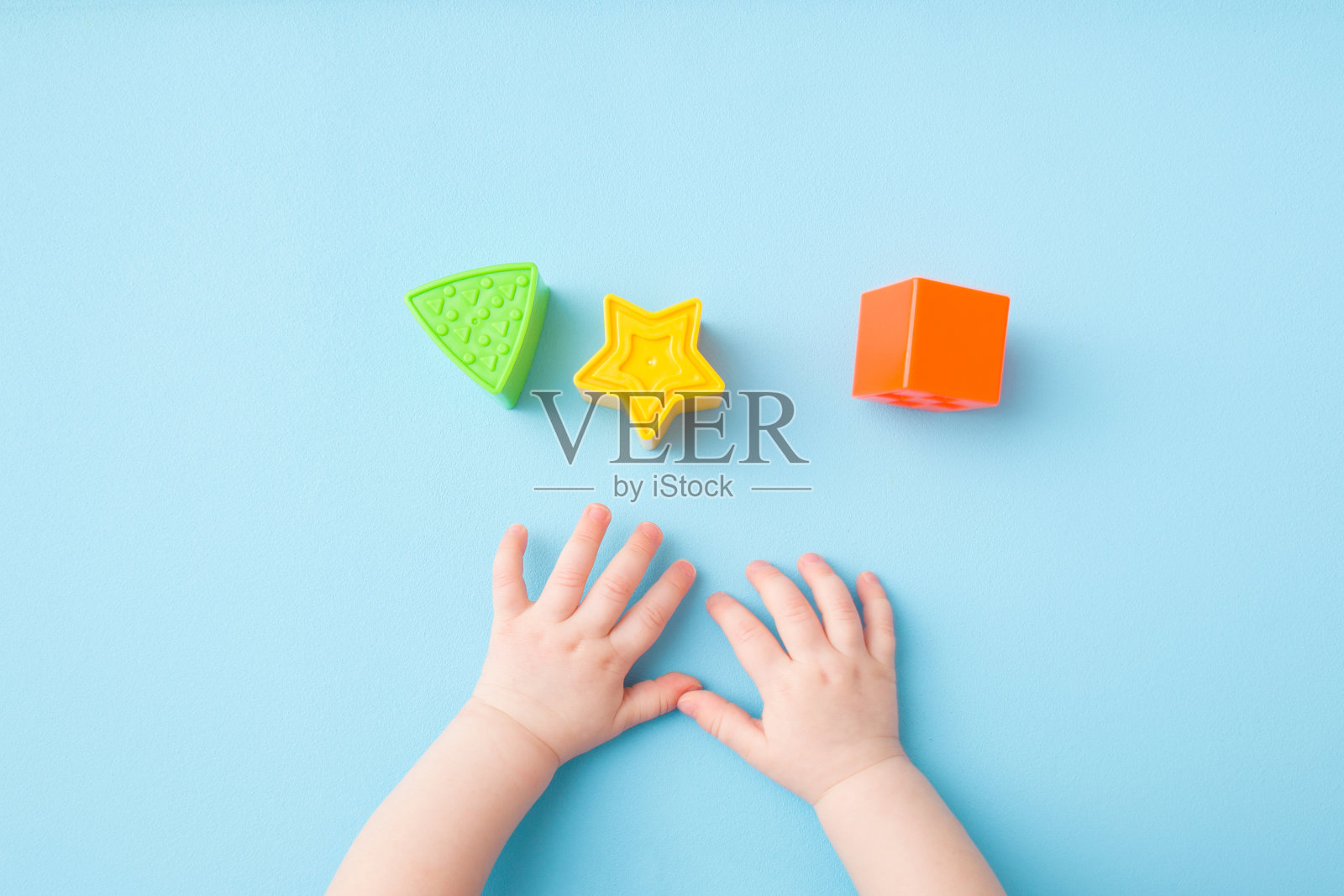 婴儿的手玩绿色的三角形，黄色的星星和橙色的方形在浅蓝色的背景。柔和的颜色。特写镜头。给小孩子的发展玩具。自顶向下的观点。照片摄影图片