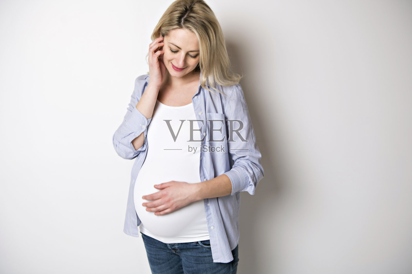 孕妇轻抚她的腹部在白色的背景照片摄影图片
