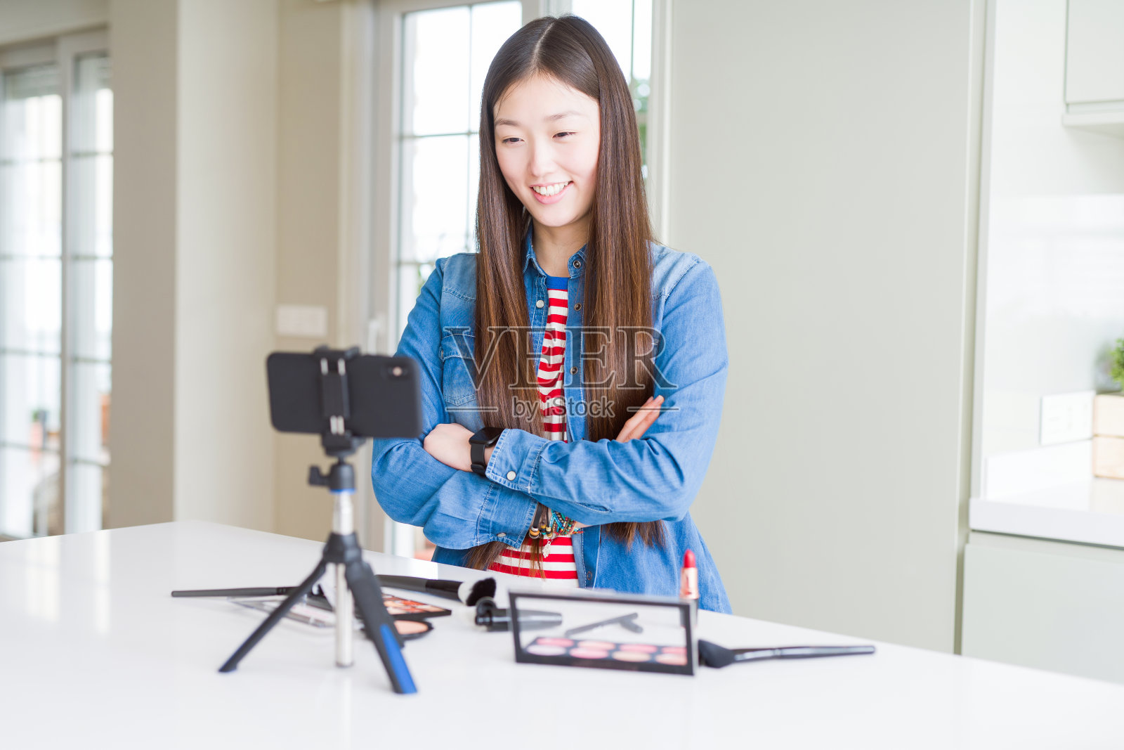 美丽的亚洲影响女人记录化妆教程使用智能手机摄像头快乐的脸微笑，双臂交叉看着镜头。积极的人。照片摄影图片