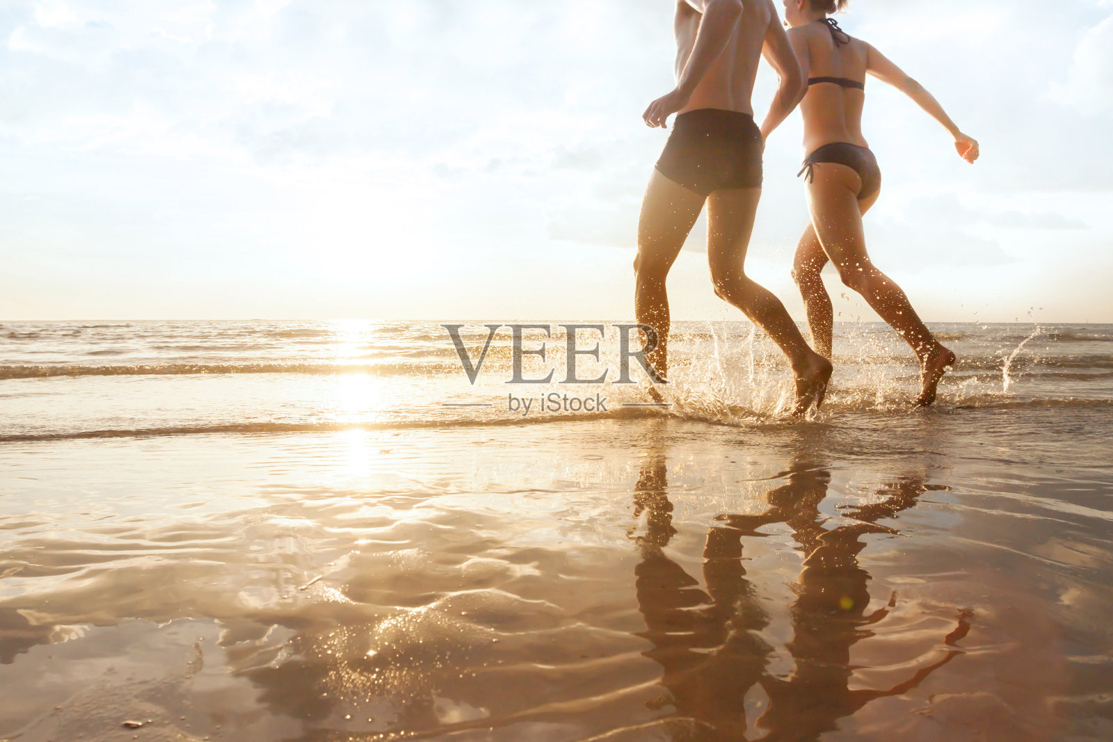幸福的年轻夫妇奔向海边，在日落的海滩上，剪影照片摄影图片