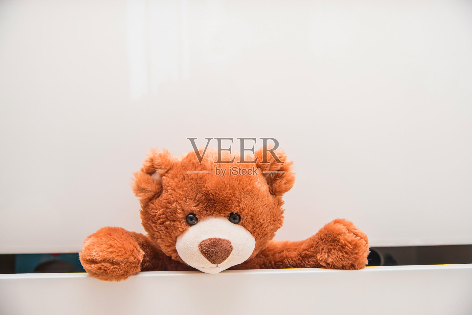 棕色毛绒玩具泰迪熊从白色抽屉的衣柜里爬出来照片摄影图片
