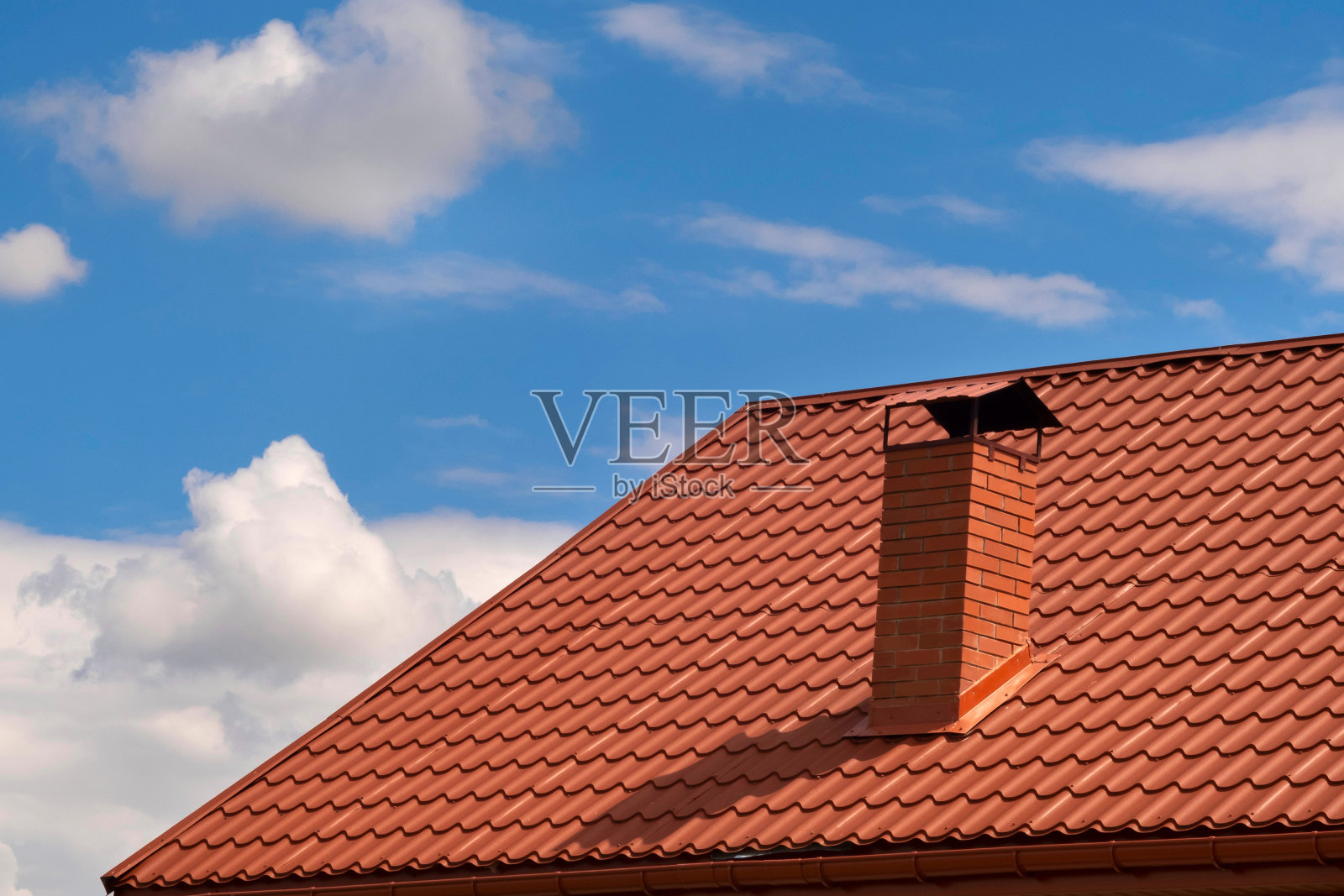 房子的一部分有一个棕色的瓦屋顶和一个烟囱，映衬着天空。金属屋顶。照片摄影图片