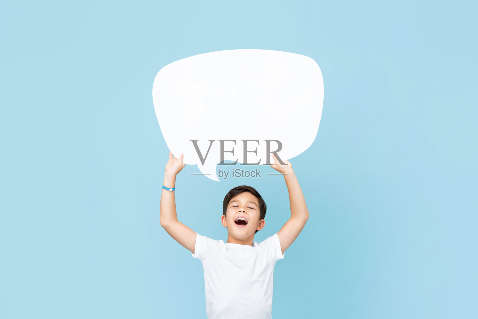 腰上的肖像微笑亚洲男孩举起一个空的白色讲话气泡在浅蓝色工作室背景照片摄影图片