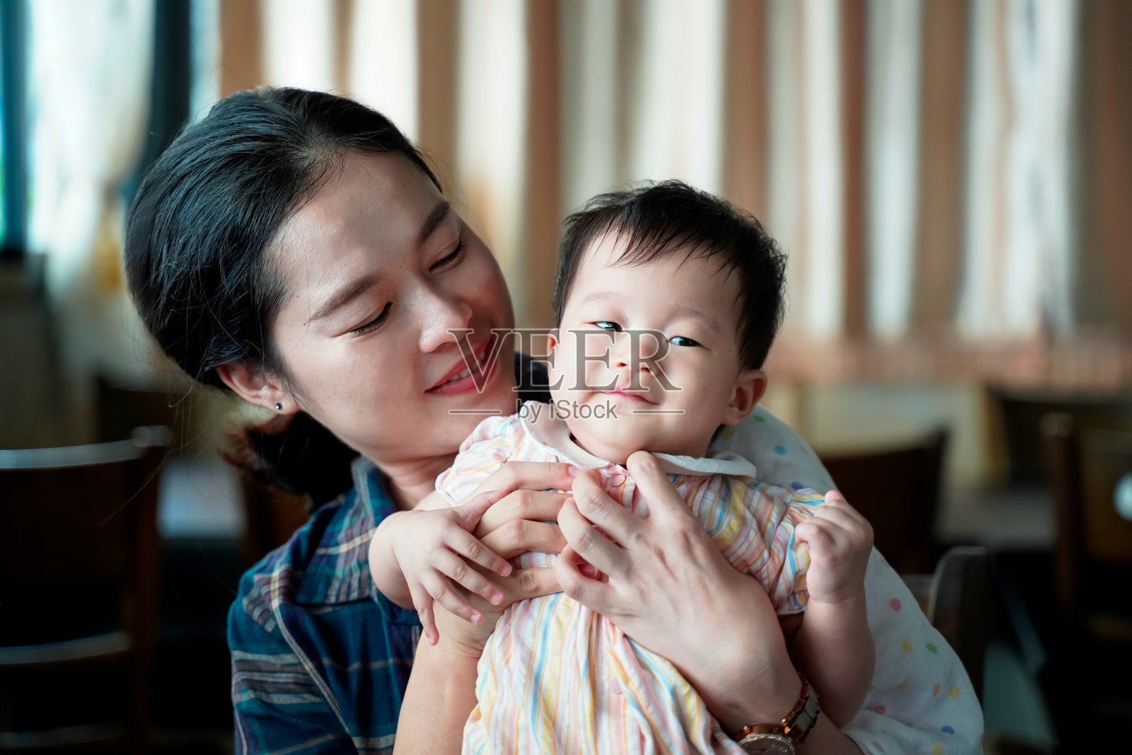 亚洲可爱的年轻妈妈一边抱着女儿一边笑着对着家里的背景，宝宝也笑着感觉这么有趣和幸福。照片摄影图片