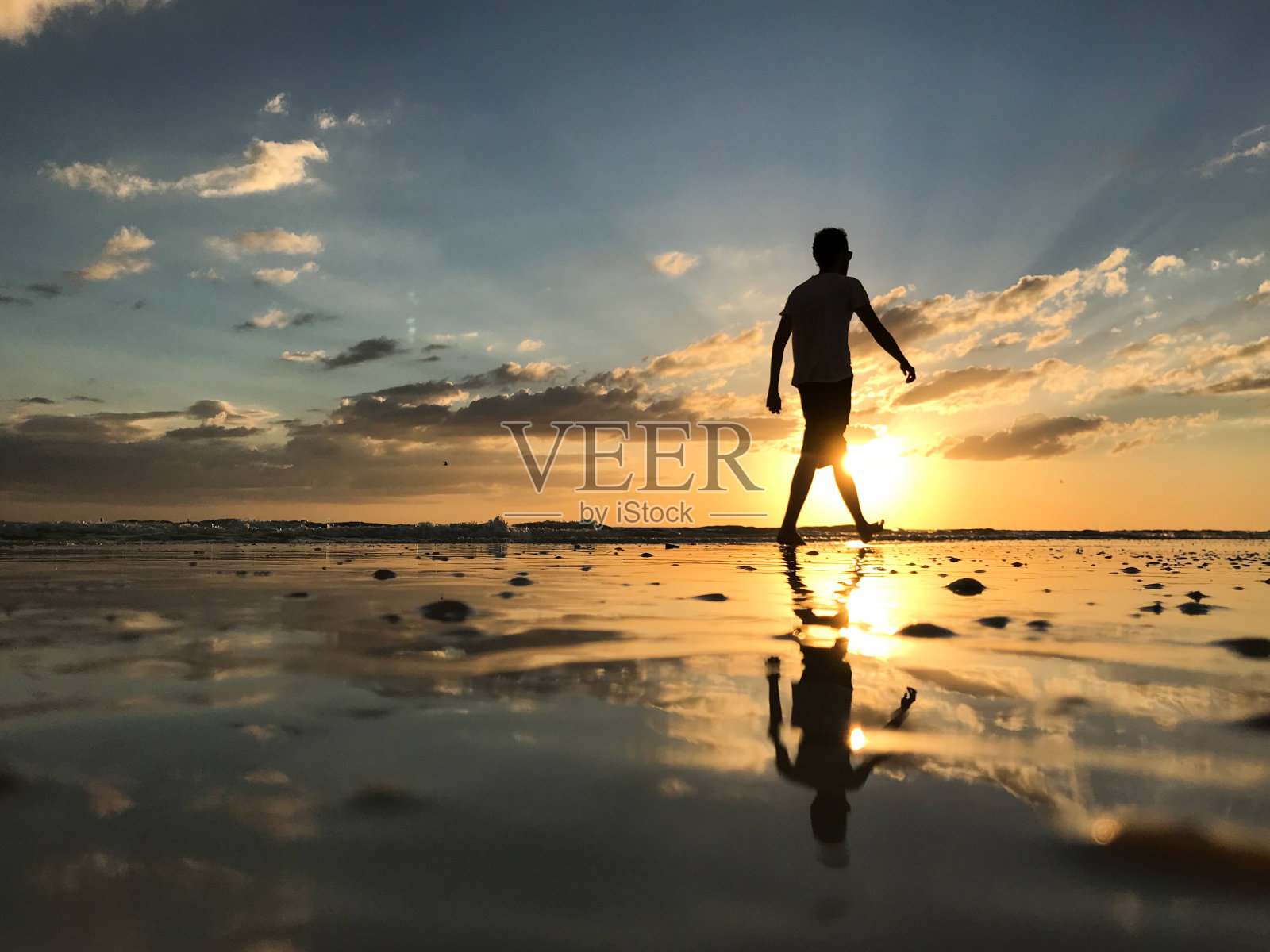 夕阳西下时，海滩上一个男人走在太阳前的剪影照片摄影图片
