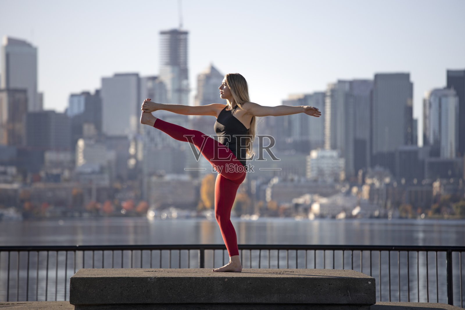 美丽的女人站立瑜伽姿势旋转伸展手到脚在城市天际线前照片摄影图片