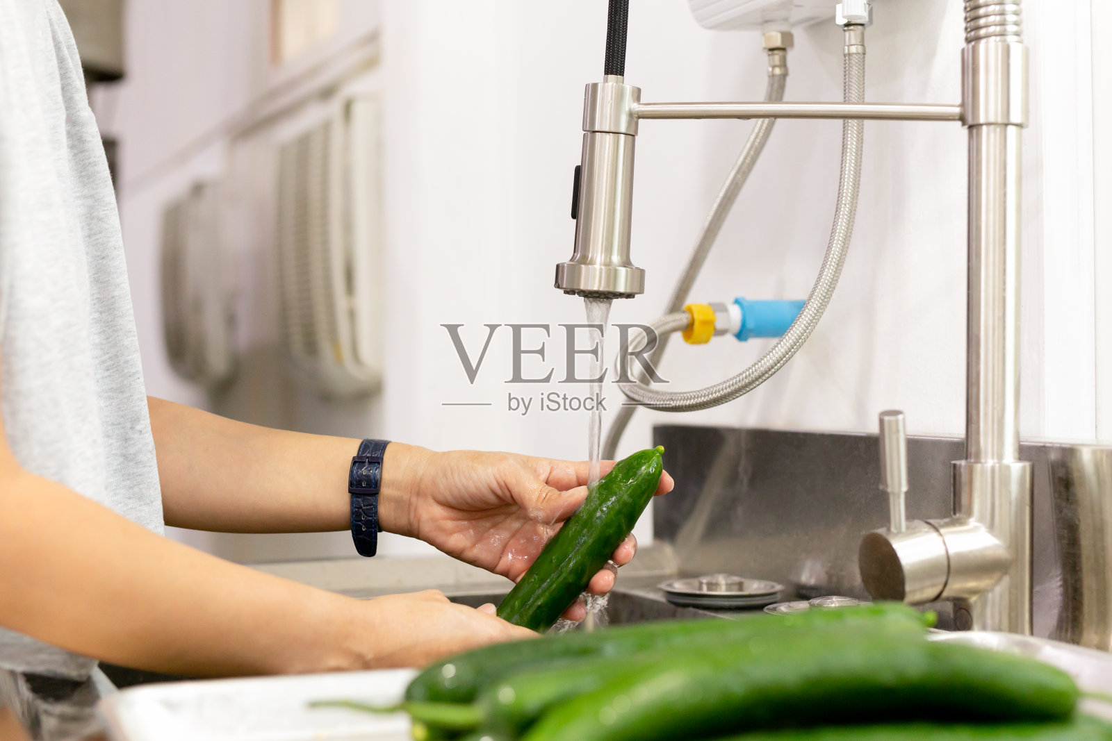 在厨房水槽里用自来水洗黄瓜的女人。照片摄影图片