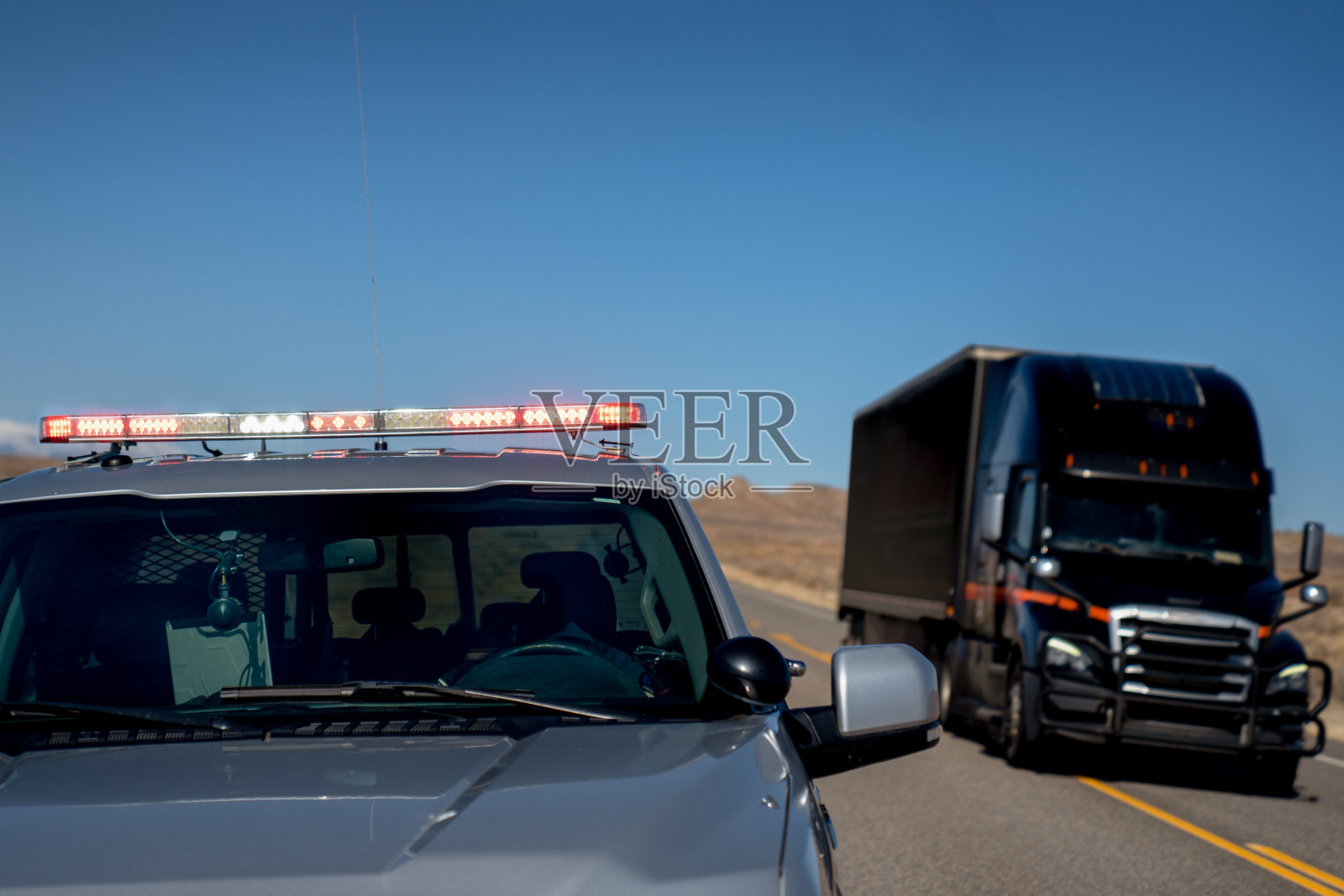 犹他州高速公路上的一辆巡逻车灯亮着，一辆半挂车开过，让一名司机靠边停车照片摄影图片