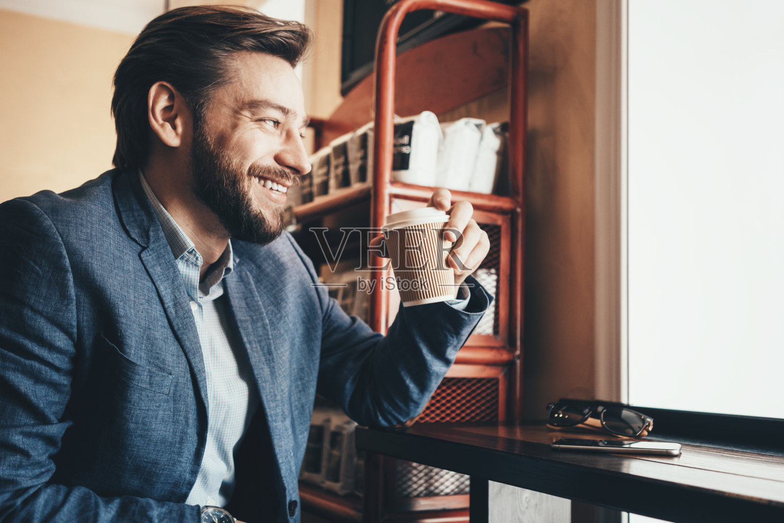 微笑的男人在城市的咖啡馆与手机和一杯咖啡照片摄影图片