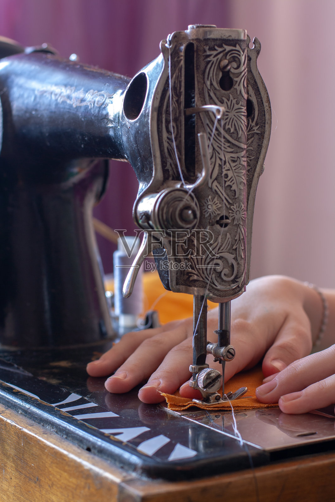 女裁缝在老式缝纫机上缝纫。景深浅。专注于针和织物。垂直的。照片摄影图片