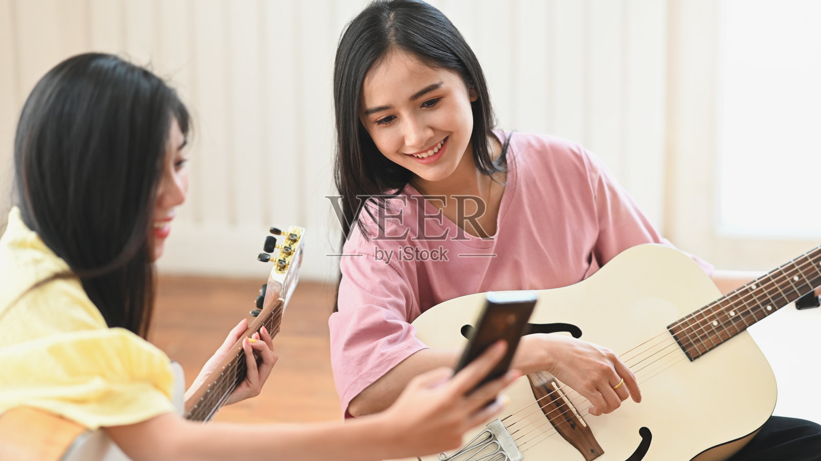 这张照片是年轻女性在舒适的客厅/音乐工作室的背景下，一起坐在木质的一楼，教/学习弹原声吉他。照片摄影图片