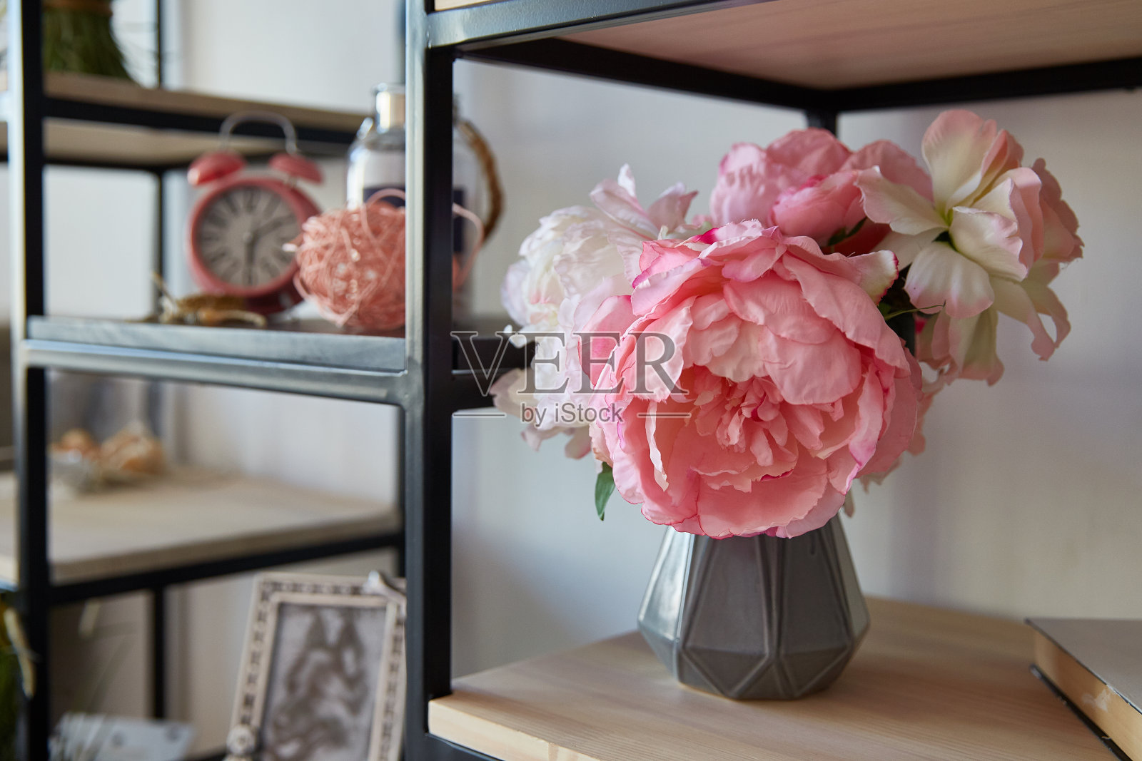 房间里的架子上有一只花瓶，上面插着粉红色的花，上面还有一个闹钟。室内设计元素照片摄影图片