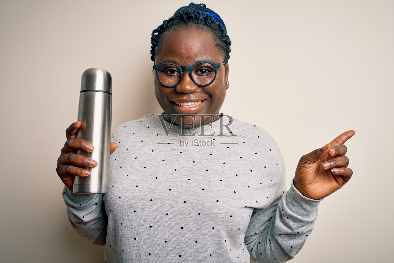 年轻的非洲裔美国人加大尺寸的女人与辫子拿着热与咖啡非常高兴地用手和手指指向一边照片摄影图片