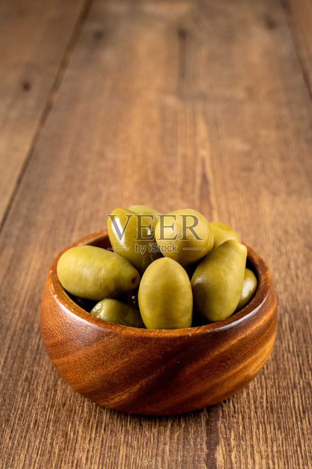 一个小木碗里，橄榄油里的绿橄榄，背景是质朴的木头照片摄影图片