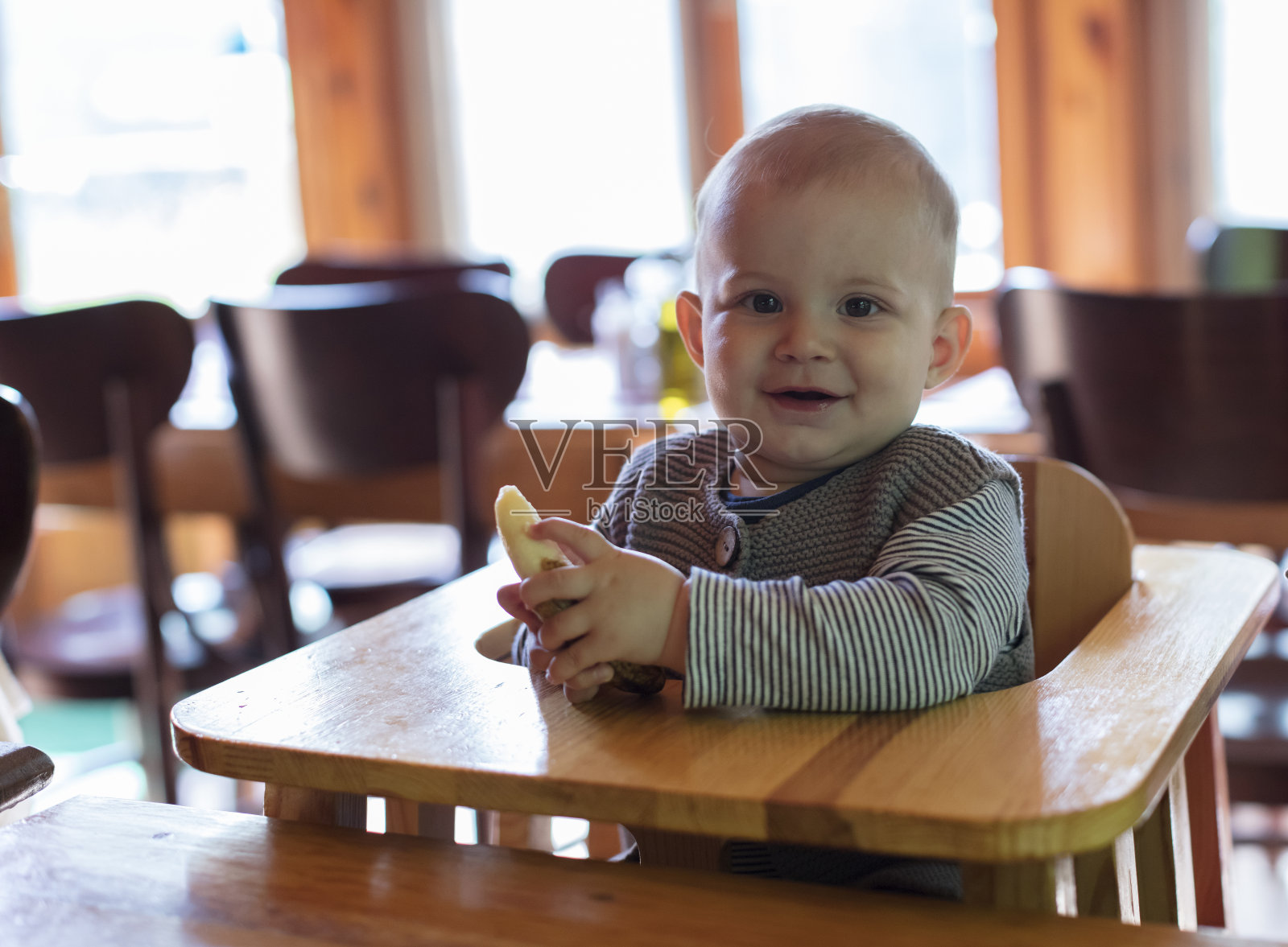 9个月大的男婴坐在高高的儿童椅上，独自在厨房里吃水果照片摄影图片