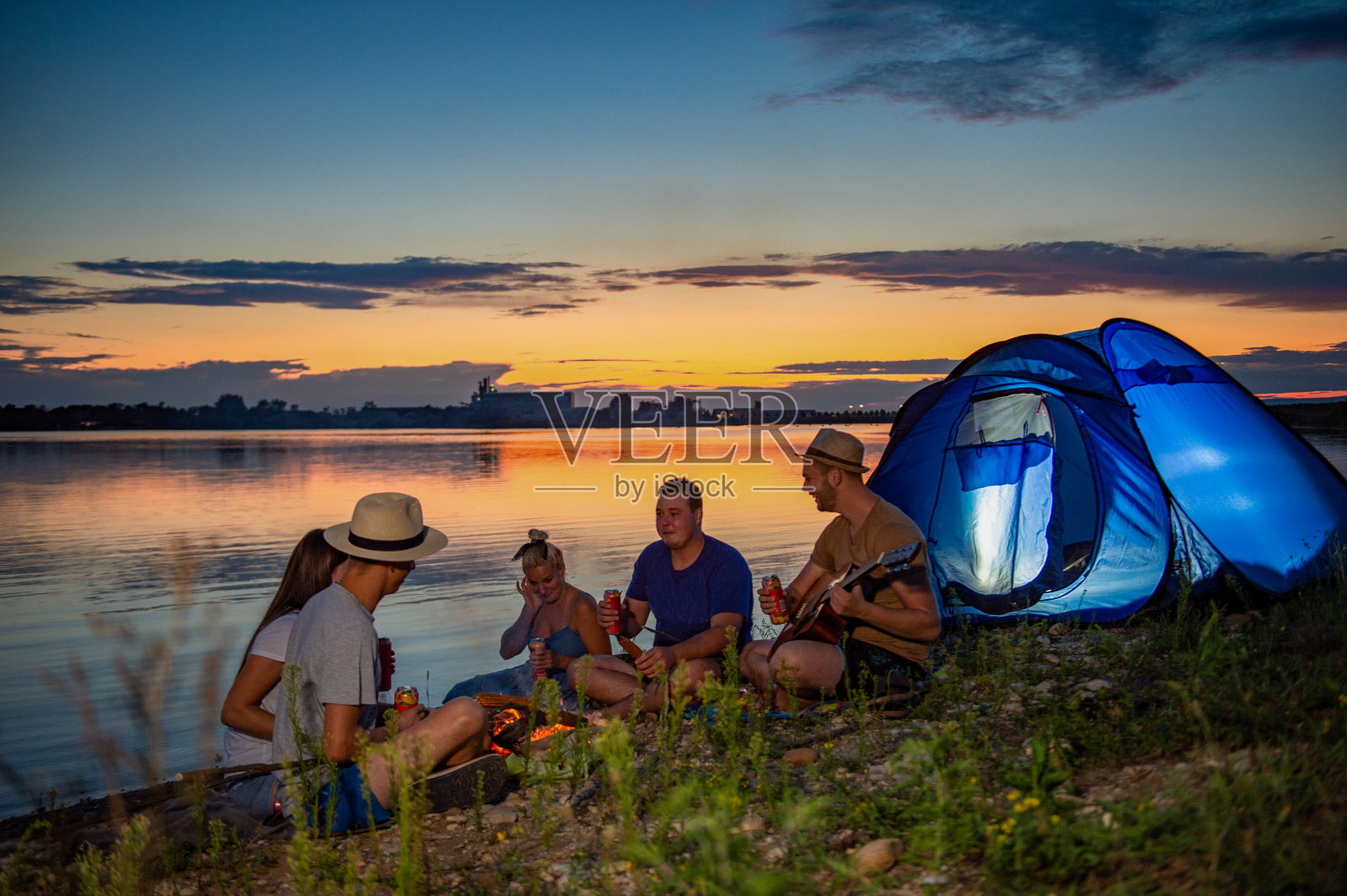 日落时分，朋友们围坐在湖边的篝火旁露营照片摄影图片