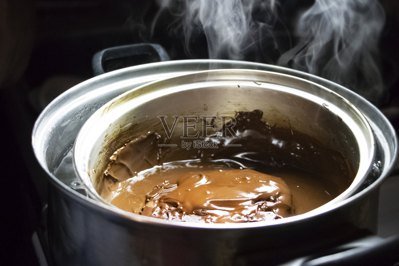 把融化的巧克力放在平底锅里，放在水浴下。在自己的厨房里做热巧克力照片摄影图片