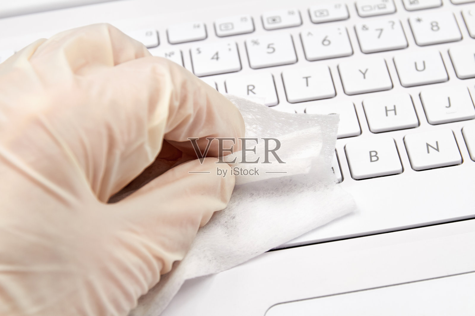 人手戴白色防护手套，用消毒布擦拭笔记本表面，预防冠状病毒、细菌、病毒和细菌。特写镜头,有选择性的重点照片摄影图片