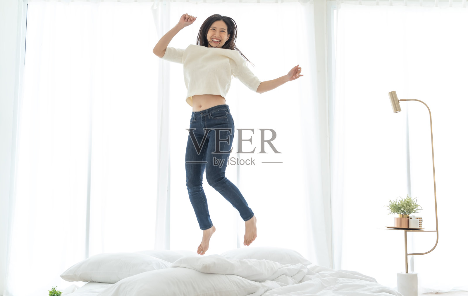 快乐的亚洲女人在床上跳。幸福的概念照片摄影图片