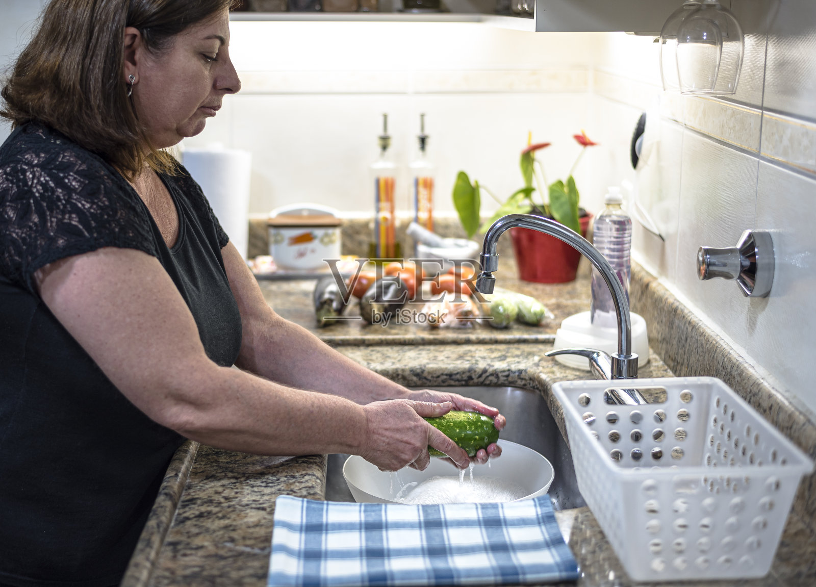 成年妇女在家庭厨房里洗蔬菜，然后把它们放进冰箱照片摄影图片