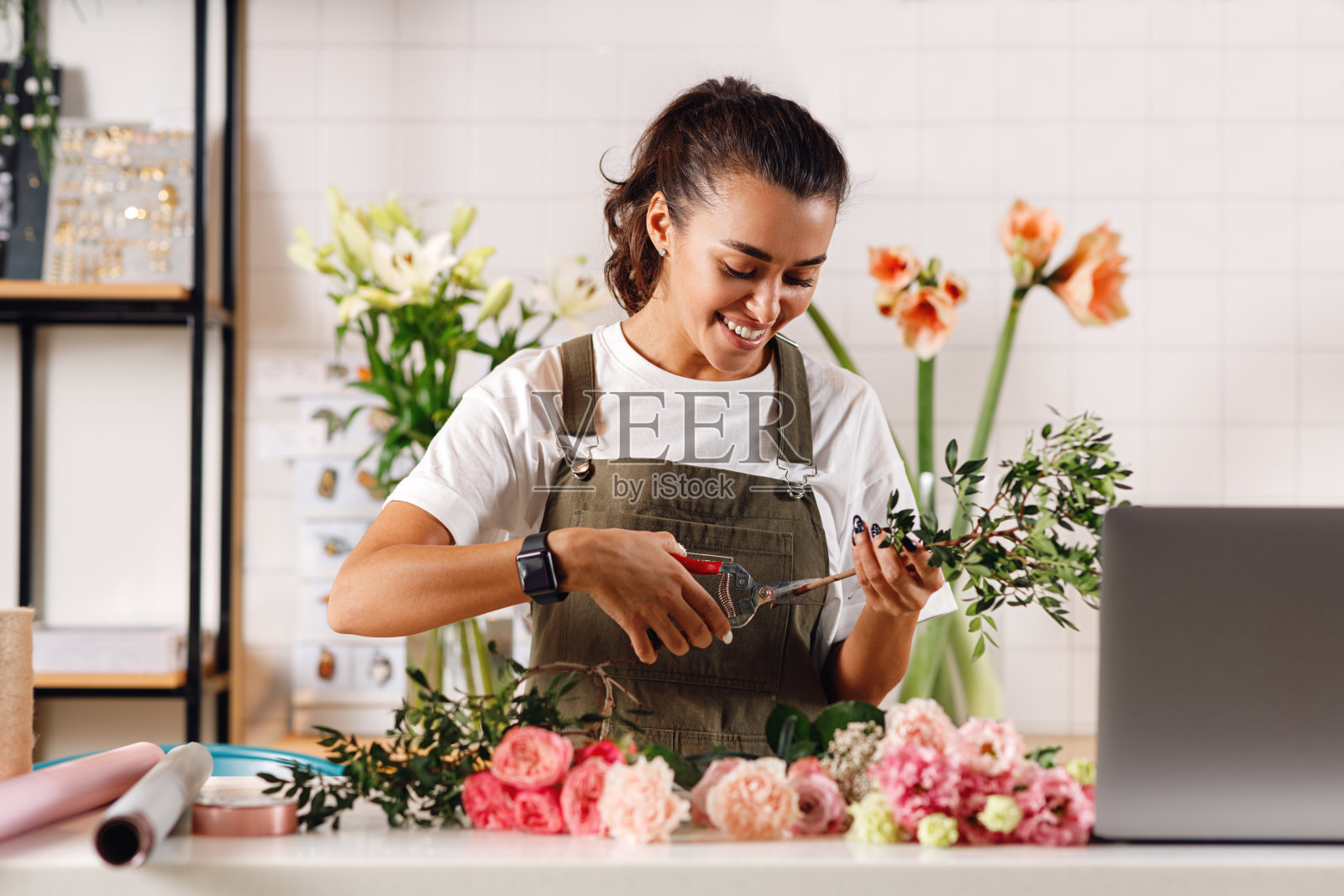 微笑的女人在柜台工作。女花匠用剪刀剪花。照片摄影图片