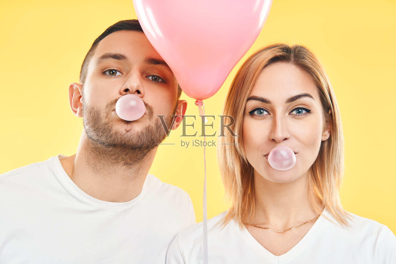 年轻的夫妇吹着泡泡糖，拿着粉红色的气球照片摄影图片