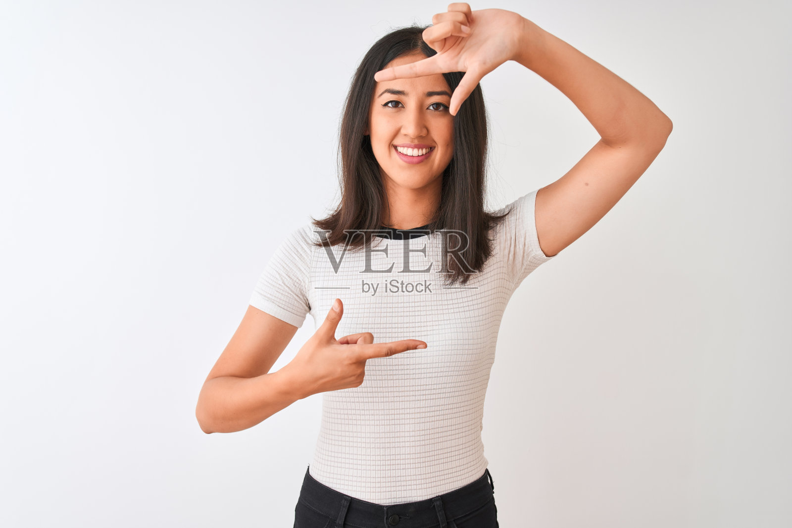 年轻美丽的中国女人穿着休闲t恤站在孤立的白色背景微笑做框架与手和手指与幸福的脸。创意和摄影概念。照片摄影图片