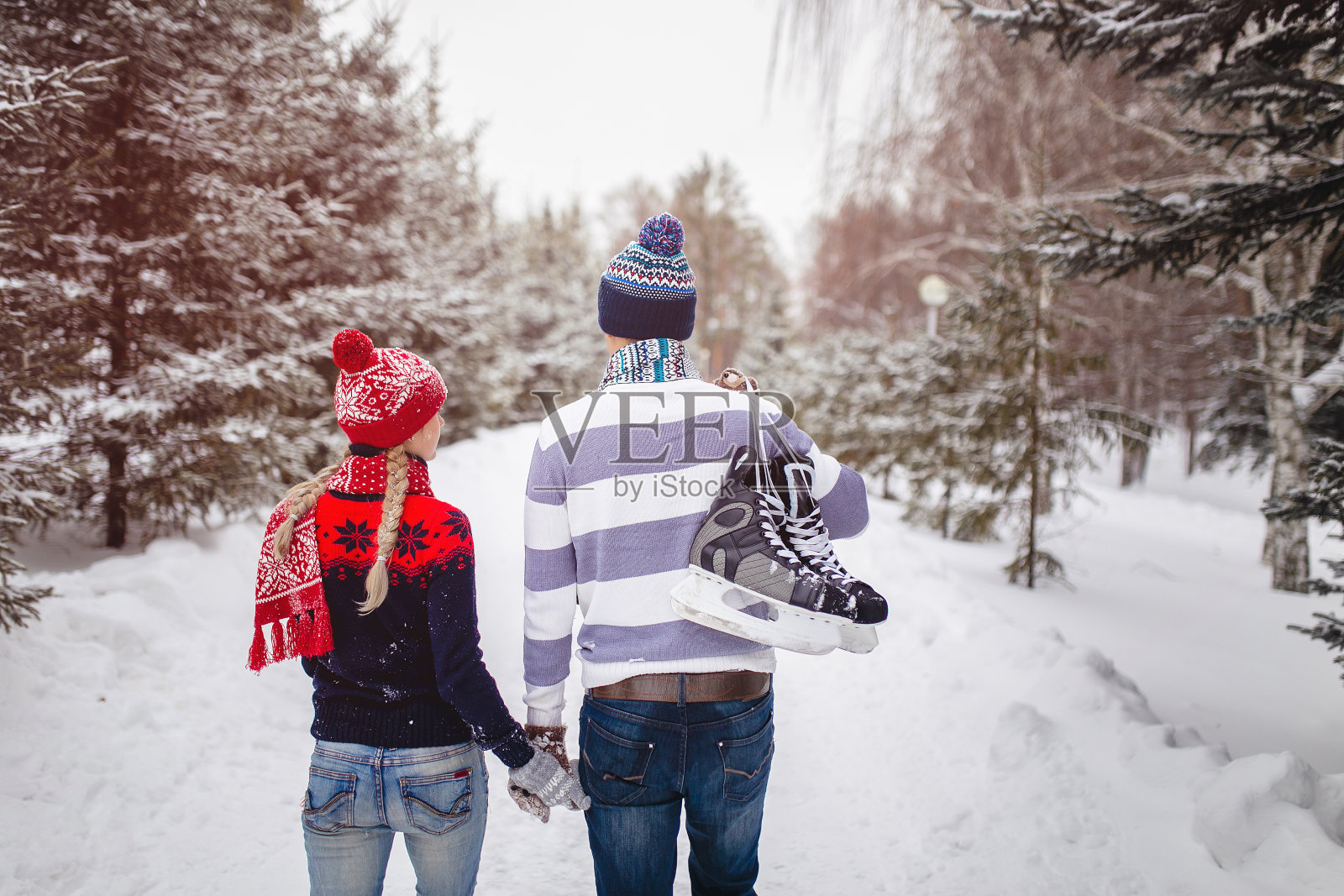 一对恩爱的情侣在冬天的公园里散步约会。一个人的背上挂着一双溜冰鞋照片摄影图片