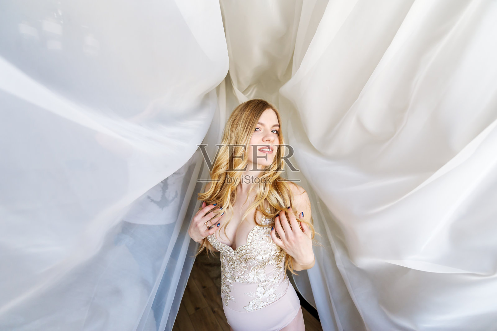 身穿内衣的孕妇在白色窗帘的背景下摆姿势。照片摄影图片