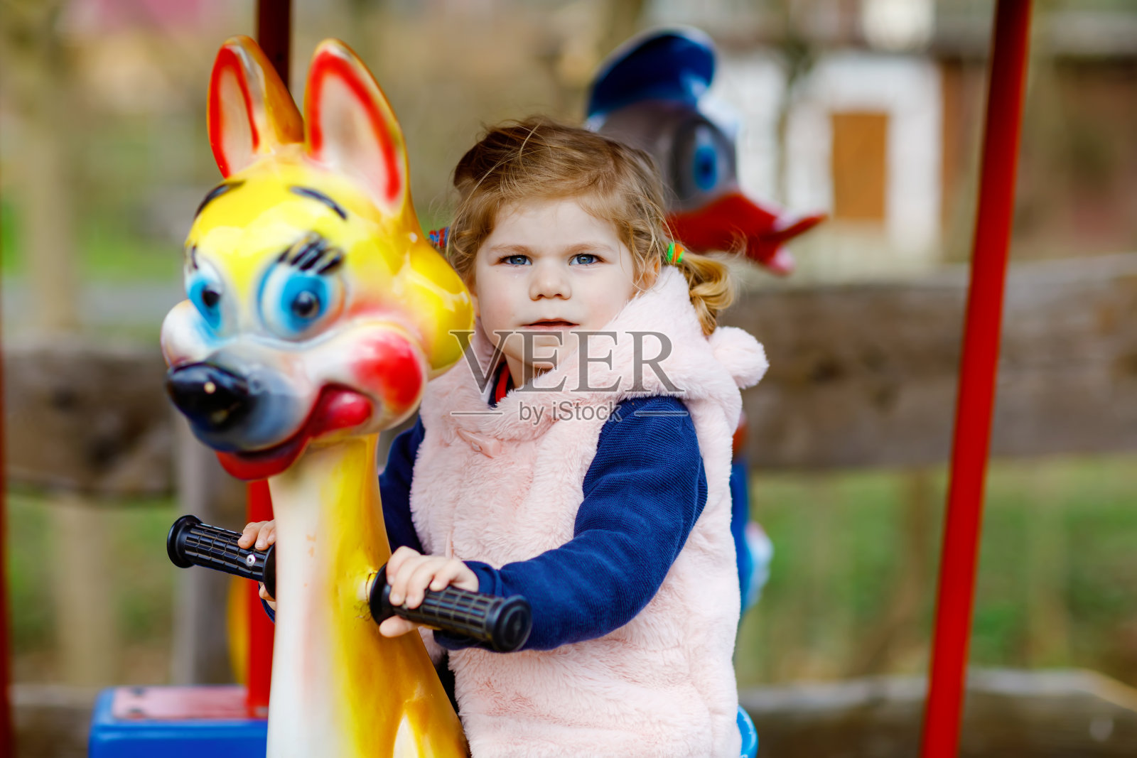 可爱的小女孩骑在动物在游乐场旋转木马。在阳光明媚的日子里，快乐健康的宝宝在户外玩耍。家庭周末或假期照片摄影图片