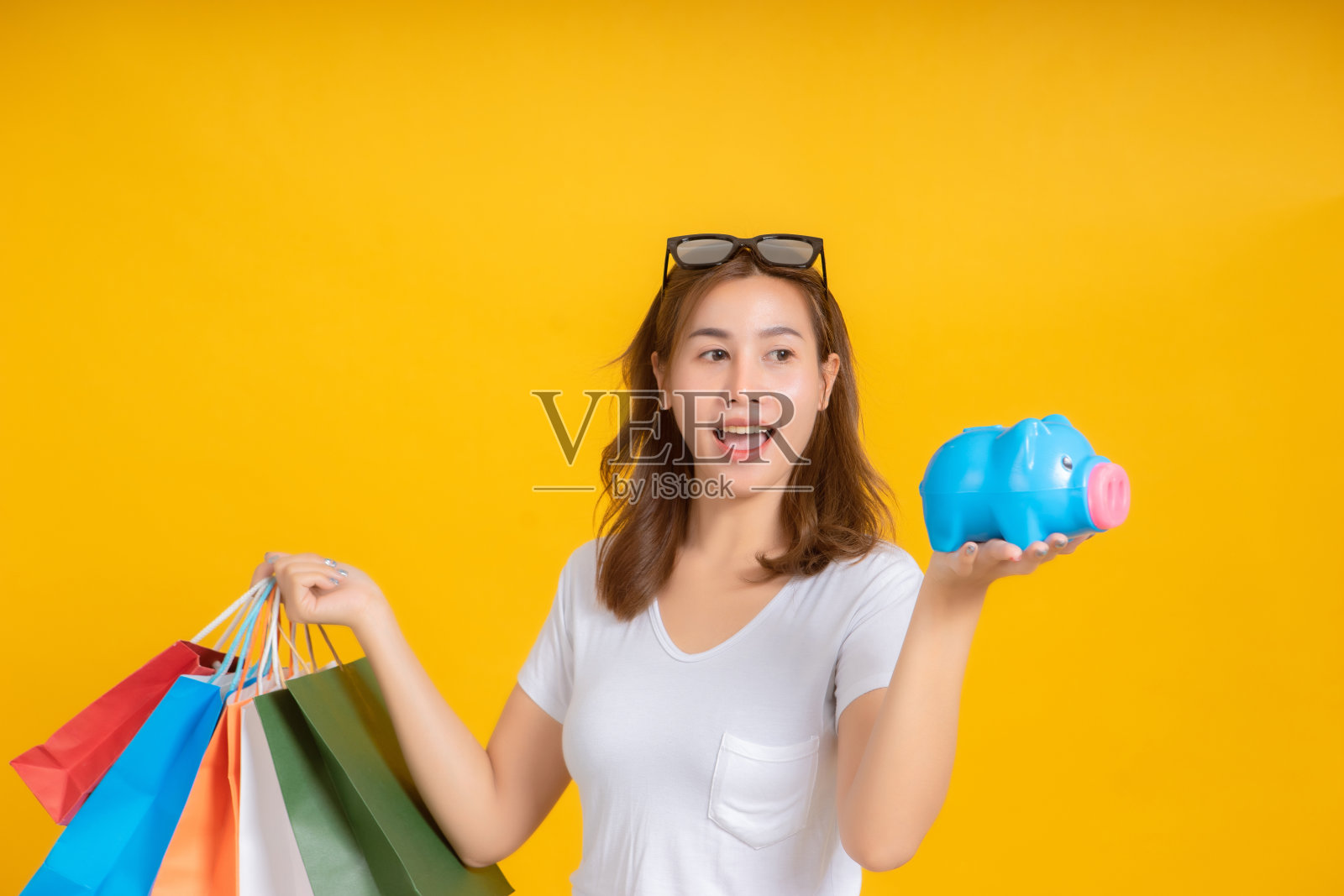 肖像快乐年轻的亚洲女人抱着存钱罐购物积极的情绪在白色t恤，黄色背景孤立的工作室拍摄和复制空间。照片摄影图片