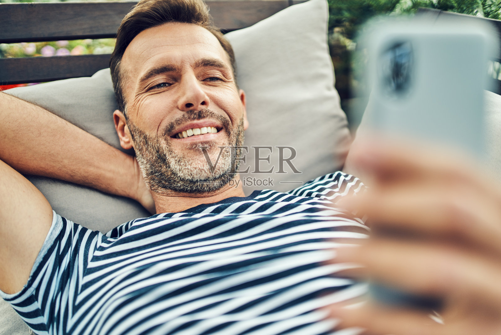 微笑的男人使用智能手机，同时放松在阳台照片摄影图片