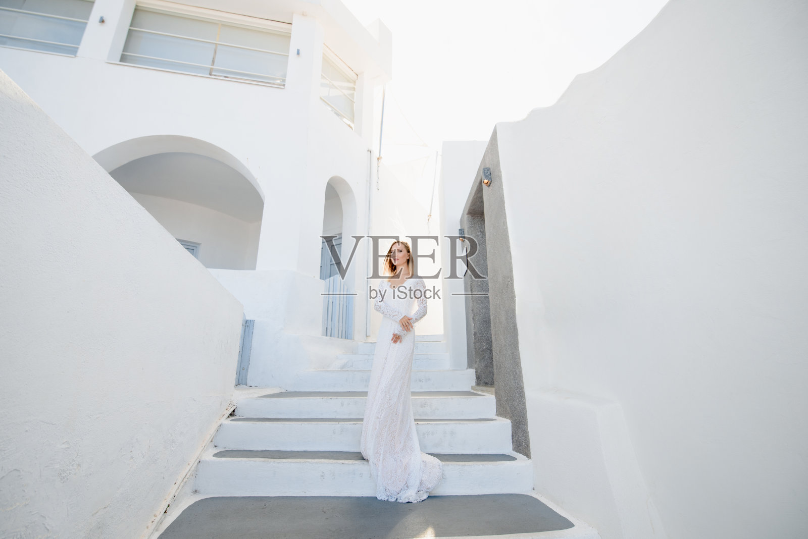 在希腊的圣托里尼，美丽的金发年轻女子穿着白色的婚纱，穿着性感的婚纱照片摄影图片