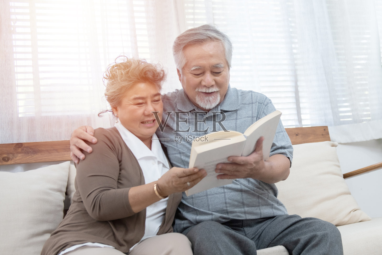 一对年老的亚洲夫妇坐在沙发上一起看书。退休后的祖母和祖父一起呆在家里。照片摄影图片