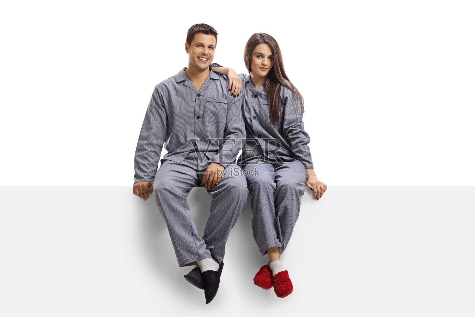 年轻夫妇穿着同样的睡衣，坐在一块空白的面板上照片摄影图片